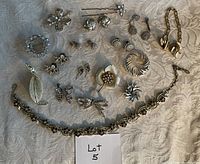 Top view of the full collection of vintage jewelry including brooches, earrings, necklaces, and sweater clip on a white patterned fabric background.