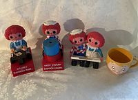 Four Raggedy Ann and Andy themed items, including two pencil sharpeners, salt and pepper shakers, and a yellow cup.