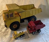 Lot of 3 vintage Tonka trucks including large yellow dump truck, medium red dump truck, and small yellow truck, all showing wear consistent with age.