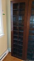 Full view of the tall wooden CD storage unit showing all 22 cubbies and its dark brown finish, positioned near a window.