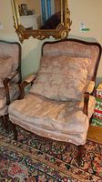 Frontal view of upholstered armchair with cushion beneath a wall mirror.