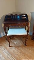 Full view of the wood desk and upholstered stool with the seat detached.