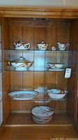 Full cabinet view showing all dishes including teapot, cream and sugar dishes, gravy boat, serving bowls, and dinner plates stacked at bottom