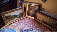 Three framed artworks leaning against wall on patterned rug