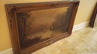 Framed landscape painting leaning against wall showing full painting and frame