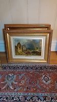 Two wood framed prints stacked on patterned rug, one showing a medieval ruin scene