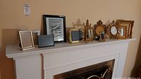 Wide view showing twelve assorted picture frames arranged on a white shelf against a tan wall, including ornate gold frames and black frames.