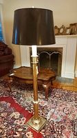 Full view of vintage floor lamp, brass base and column with dark brown shade, placed on floral rug with fireplace and furniture in background