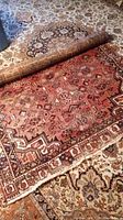 Rug partially rolled to show overall pattern and border on top of larger patterned carpet