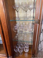 Full view of cabinet showing three shelves of various glass stemware: martini glasses on top, smaller wine glasses in middle, and larger bowl wine glasses on bottom shelf.
