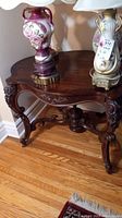 Front view of antique wooden side table with two lamps on top, showing carved curved legs and scalloped tabletop.