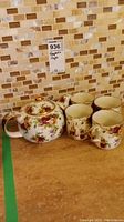 Teapot and 4 tea cups displayed together on kitchen counter with tile backsplash.