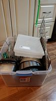 Photo of bin filled with various metal bakeware items including loaf pans, bundt pan, muffin tray, clear plastic containers with lids.