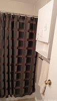 Medicine cabinet mounted on bathroom wall above a towel holder and next to shower curtain with geometric plaid pattern.