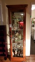 Front view of lighted wooden display cabinet filled with collectibles, showing glass door and interior shelves.
