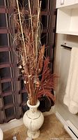 Tall floral arrangement with dried branches and feathers inside carved white vase