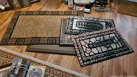 Fatigue mat with natural fiber look and black geometric border alongside two smaller 'Welcome' mats with mosaic patterns.