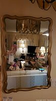 Full view of the gold tone framed mirror hanging on wall, showing room reflection and frame shape.