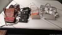 Wide-angle photo showing most of the handbags and clutches including various colors and styles: brown, black, beige, orange, and silver bags laid out on a bed.