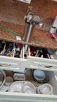 Wide view showing counter with stainless steel utensil holder and lower drawers containing utensils and bowls.