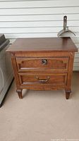 Front view of wooden side table showing two drawers with decorative metal handles and carved legs.