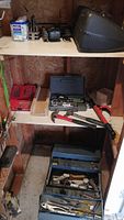 Wooden shelving unit holding assorted tool cases and tools, including a red tool box, a black tool case, hammers, and large red pipe wrench