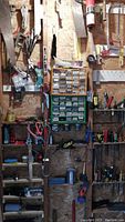 Wide view of tools arranged on a wooden wall in a shed, showing boxes of screws and nails and various hanging tools.