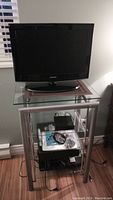 Samsung 22 inch TV sitting on glass and metal stand with electronic players below.