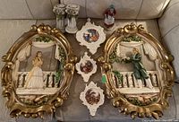 Wide shot of the vintage set including two large ornate oval plaques showing courting scenes, three smaller decorative plaques, a figurine of a woman, and a pair of small column ornaments.