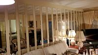 Seventeen tall narrow mirrors mounted vertically on wall behind couch with lamps and furniture reflected.