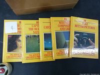 Six Kodak photography books lined up, showing yellow covers with titles and photo images, stacked on the floor with a cardboard box behind
