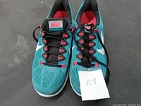 Top-down view of pair of teal Nike running shoes with black laces and red accents. Size 9.5 indicated on note.