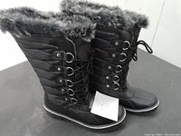 Front and side view of the black ladies winter boots showing the quilted upper, lace-up metal eyelets, and faux fur trim.