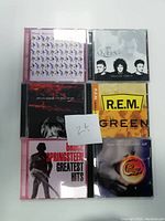 Photo showing six CD jewel cases stacked in two rows of three. Album covers visible for The Rolling Stones, Queen, Adam Adams, R.E.M., Bruce Springsteen, and Chicago.