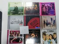Photo of 9 music CDs arranged in a 3x3 grid showing album covers and artist names.