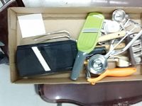 Box of assorted used kitchen tools and gadgets including slicers, measuring spoons and can opener.