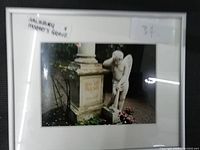 Framed photo with image of Mozart's tombstone and angel statue in a garden setting, with flowers at the base.