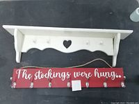 White wooden wall shelf with hooks and heart cutout; red wooden hook rack with 'The stockings were hung...' text