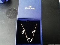 Swarovski necklace and earrings inside blue Swarovski box showing design details of heart and infinity symbols with crystals.