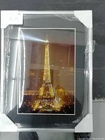 Photo of a framed Eiffel Tower nighttime photo print protected with plastic wrapping and corner protectors.