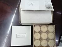 Box with 12 white scented tea light candles from The White Company London, partially opened to show the candle arrangement.