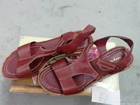 Top and side view of red leather women's sandals sitting on box showing the design, size and upper straps