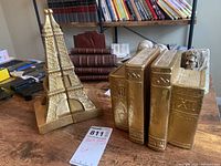 All four gold foil bookends displayed, two shaped as Eiffel Tower and two shaped as stacked books with Roman numerals.