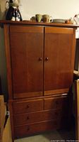 Front view of the Thomasville armoire showing two doors and four drawers below.