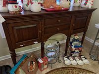 Front view of wooden buffet showing drawers, cabinets, carved legs, and white scratches on edge of tabletop. Decorative items on top and some items displayed under and around buffet.