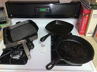 Three cast iron skillets and one Calphalon pan arranged on stove and counter, viewed from above.