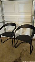 Pair of black chairs with black metal frames and leather upholstery positioned side by side in garage area.
