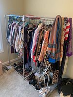 Photo showing women's tops, jackets, pants hanging on a metal rack with assorted patterns and colors. Shoes are placed at the bottom of the rack.