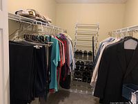 Closet with men's dress pants, polo shirts, button-ups hanging on racks with men's dress shoes on a rack in back.