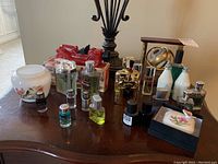 Overview photo showing lot items arranged on wooden surface, includes floral china bowl, red ceramic car trinket, award with clock and globe, multiple cologne bottles and trinket box.